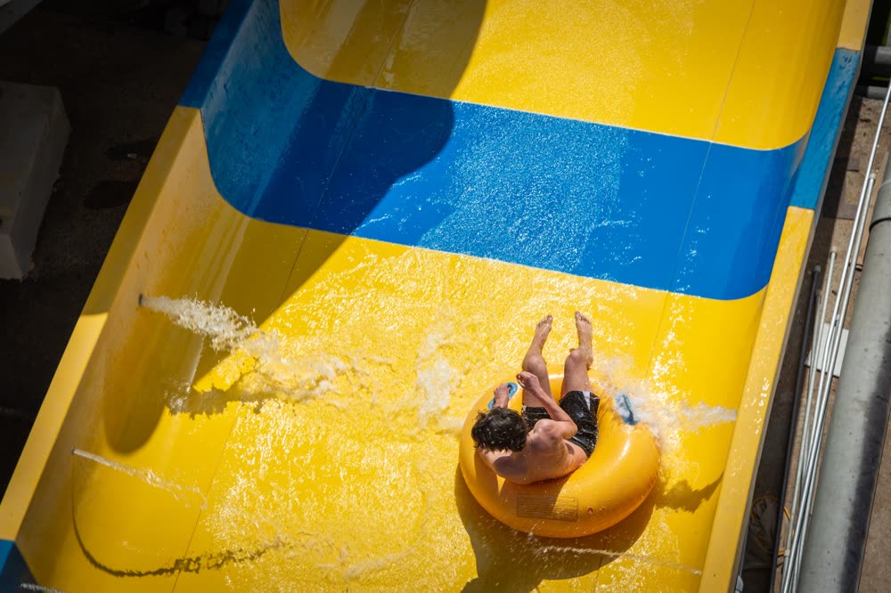Person rutscht mit einem Reifen eine gelb-blaue Wasserrutsche hinunter