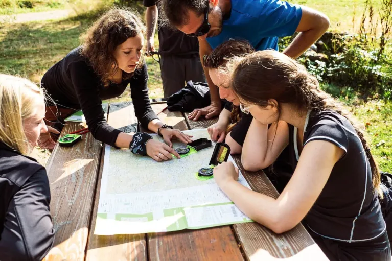 Gruppe plant beim Teamevent eine Route mit Karte und Kompass